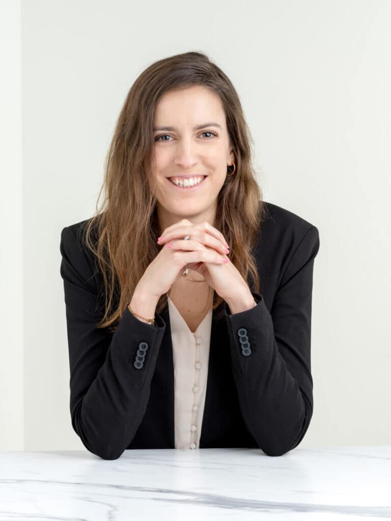 Femme professionnelle souriante : portrait business Femme professionnelle souriante en blazer noir et chemisier. Assise à un bureau en marbre, les mains croisées, elle regarde l'objectif.